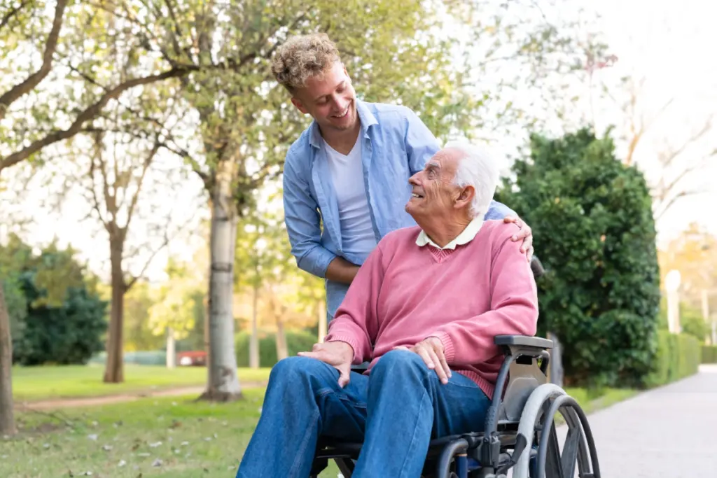Alter Mann im Rollstuhl wird von jungem Mann begleitet als Symbolbild für Seminare zum Thema Kommunikation am Lebensende